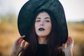 Portrait of a beautiful girl with pale skin and black lips in a big black hat. Woman in the image of a witch for Halloween. Royalty Free Stock Photo