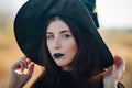 Portrait of a beautiful girl with pale skin and black lips in a big black hat. Woman in the image of a witch for Halloween. Royalty Free Stock Photo