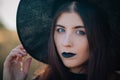 Portrait of a beautiful girl with pale skin and black lips in a big black hat. Woman in the image of a witch for Halloween. Royalty Free Stock Photo