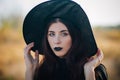 Portrait of a beautiful girl with pale skin and black lips in a big black hat. Woman in the image of a witch for Halloween. Royalty Free Stock Photo