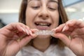 Portrait of beautiful girl patient holding orthodontic retainers aligners in dental clinic.