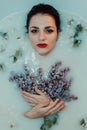 Portrait of a beautiful girl with red lipstick and makeup relaxing and resting in the bath with milk and lilac Royalty Free Stock Photo
