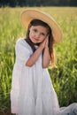 portrait of a beautiful girl in a straw hat standing in a field with green grass at sunset and looking the camera Royalty Free Stock Photo