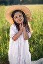 portrait of a beautiful girl in a straw hat standing in a field with green grass at sunset and looking the camera Royalty Free Stock Photo