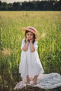 portrait of a beautiful girl in a straw hat standing in a field with green grass at sunset and looking the camera Royalty Free Stock Photo