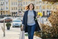 Portrait of beautiful girl walking in city, young woman with bouquet of yellow flowers and shopping bag, background spring city