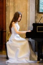 Portrait of a beautiful girl wearing white wedding dress at the piano playing