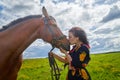 Portrait of beautiful gypsy girl with a horse on a field with green glass in summer day and blue sky and white clouds background. Royalty Free Stock Photo
