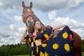 Portrait of beautiful gypsy girl with a horse on a field with green glass in summer day and blue sky and white clouds background. Royalty Free Stock Photo