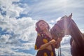 Portrait of beautiful gypsy girl with a horse on a field with green glass in summer day and blue sky and white clouds background. Royalty Free Stock Photo