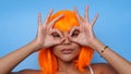 Portrait of beautiful happy Asian woman in bright orange wig posing over blue Royalty Free Stock Photo