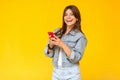 Portrait of beautiful happy brunette young woman with makeup in denim casual style standing, holding her red smart mobile phone, Royalty Free Stock Photo