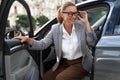 Portrait of a beautiful and happy business woman wearing eyeglasses getting out of her modern car and smiling. Arriving