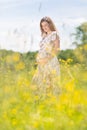 Beautiful pregnant woman in white summer dress in meadow full of yellow blooming flowers. Royalty Free Stock Photo