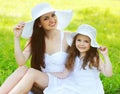 Portrait beautiful happy smiling mother with little girl child wearing a straw hat on the grass in a summer day Royalty Free Stock Photo