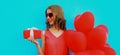 beautiful happy smiling woman holding gift box and bunch of red heart shaped balloons on a blue background Royalty Free Stock Photo
