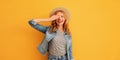 Portrait of beautiful happy surprised smiling young woman covering her eyes wearing summer straw hat, denim jacket on orange Royalty Free Stock Photo