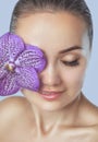 Portrait of a beautiful happy woman with clean skin and with nude make-up. She holds a beautiful purple orchid near her face. Royalty Free Stock Photo