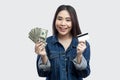 Portrait of beautiful happy young asian girl in blue denim jacket standing and holding bank credit card and many cash dollars with