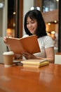 A portrait of a beautiful and happy young Asian woman enjoys reading a book at a cafe Royalty Free Stock Photo