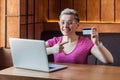 Portrait of beautiful happy young bussineswoman with short hair in pink t-shirt and eyeglasses is sitting in cafe, pointing finger