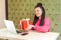 Portrait of beautiful happy young woman with black dreadlocks in pink blouse sitting in cafe, holding red present box, showing her Royalty Free Stock Photo