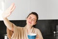 Portrait of beautiful, happy young woman covers her eyes from morning sunlight, waking up and drinking coffee, holding Royalty Free Stock Photo