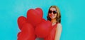 beautiful happy young woman holding bunch of red heart shaped balloons wearing a sunglasses on a blue background Royalty Free Stock Photo