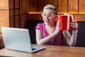 Portrait of beautiful happy young woman with short hair in pink t-shirt and eyeglasses is sitting in cafe, holding red present box Royalty Free Stock Photo