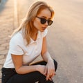 Portrait of a beautiful hipster young woman in stylish sunglasses in a white polo t-shirt in black jeans at sunset. American girl Royalty Free Stock Photo