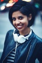 Portrait of beautiful Hispanic latino girl woman shor black hair in leather jacket with headphones outside in evening night city