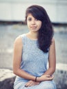 Portrait of beautiful Hispanic latino white girl woman with brown eyes, long dark curly wavy hair in gray dress sitting in park Royalty Free Stock Photo