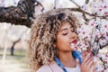 Portrait of beautiful hispanic woman with afro hair in spring smelling pink blossom flowers. nature Royalty Free Stock Photo