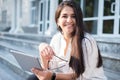 Portrait of a beautiful indian girl. Business woman smiling, holding glasses and tablet in her hands, sitting on the steps of an Royalty Free Stock Photo