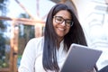 Portrait of a beautiful indian girl. Business woman, wearing glasses, smiling, sitting on the steps of an office building, holding Royalty Free Stock Photo