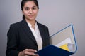 Portrait of a beautiful Indian young business woman in a business suit, holding a blue folder with documents in her hand, looking Royalty Free Stock Photo