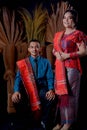 Portrait of beautiful indonesian couple wearing traditional batak costume sit on brown couch isolated on black background