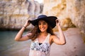 Portrait of beautiful latin girl on the beach with black hat smile neat ocean and rocks on summer vocation Royalty Free Stock Photo