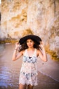 Portrait of beautiful latin girl on the beach with black hat smile neat ocean and rocks on summer vocation Royalty Free Stock Photo