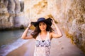 Portrait of beautiful latin girl on the beach with black hat smile neat ocean and rocks on summer vocation Royalty Free Stock Photo