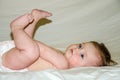 Portrait of a beautiful little baby girl is lying with his feet and holds his hand diaper looking away Royalty Free Stock Photo