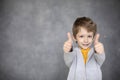 Portrait of beautiful little boy giving you thumbs up over modern gray background Royalty Free Stock Photo