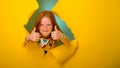 Portrait of beautiful little ginger kid girl giving you thumbs up over yellow background. breaking through yellow paper Royalty Free Stock Photo