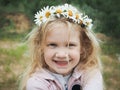 Portrait of a beautiful little girl with blond hair in a wreath of daisies. Field, green grass.