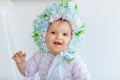 Portrait of a beautiful little girl in a bright room in a hat made of flowers