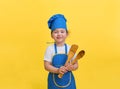 Portrait of a beautiful little girl dressed as a chef and holding a wooden spatula and spoon. Cute girl in a blue and yellow chef Royalty Free Stock Photo