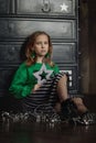 Portrait of a beautiful little girl in a fashionable New Year`s image, in a green sweatshirt and holding a gift.