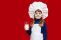 Portrait of beautiful little girl in form of cook on red drink milk