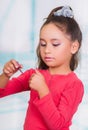 Portrait of beautiful little girl painting her nails, wearing a red blouse in a blurred background Royalty Free Stock Photo