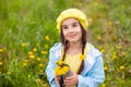 Portrait of a beautiful little girl with two pigtails holds a bouquet of yellow dandelions in a metal mug, looks up Royalty Free Stock Photo